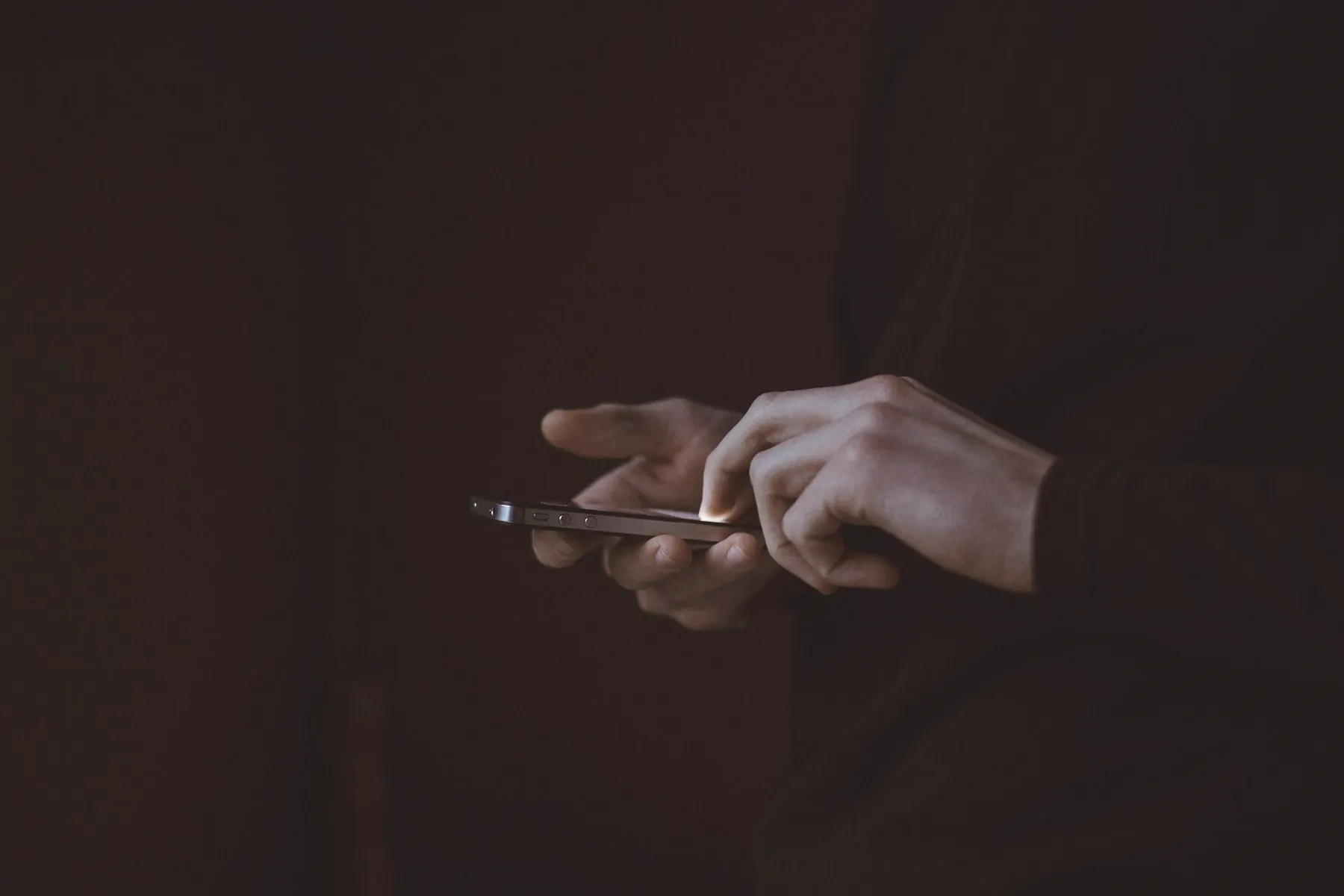 Hands holding a smartphone in a dark room, sending a private message