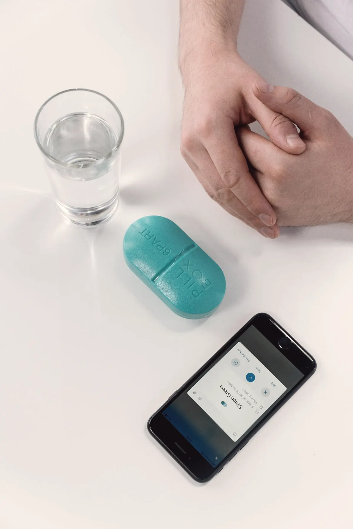 A pill case, a glass of water and a medication reminder app on a phone
