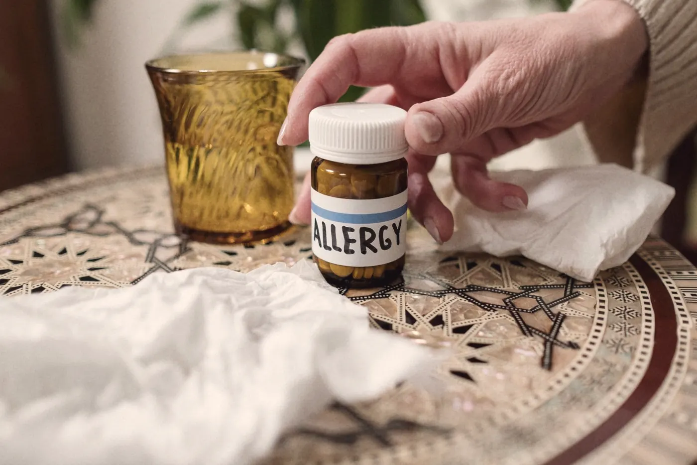 A bottle of allergy tablets beside tissues on a patterned table, a common cause of cold-like symptoms