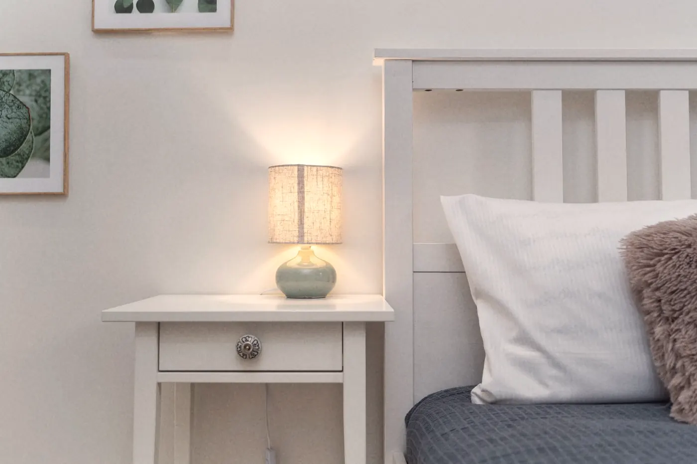 A lit lamp on a white nightstand beside a bed, for sleep changes some people notice on PEP