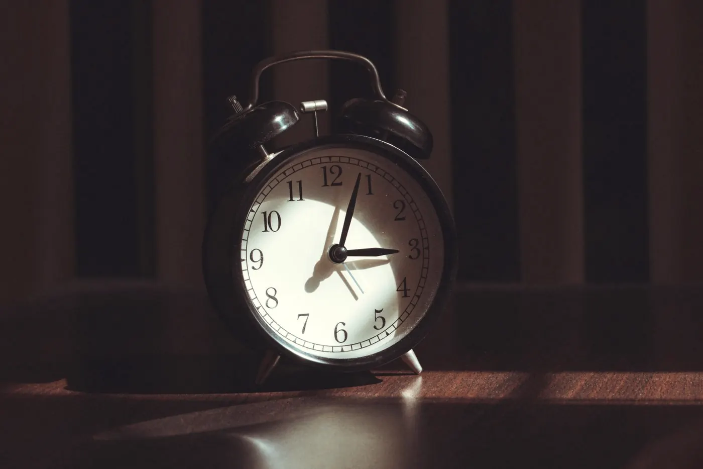 A classic black alarm clock lit by warm light on a dark table