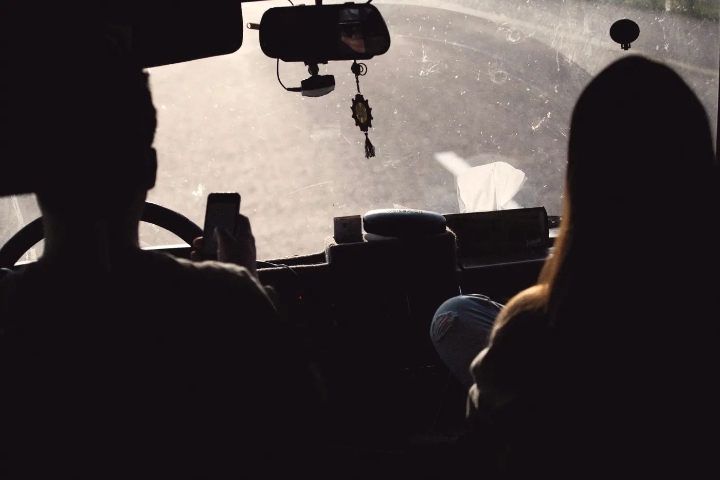 Silhouettes of a driver and a passenger looking at a smartphone inside a car at sunset
