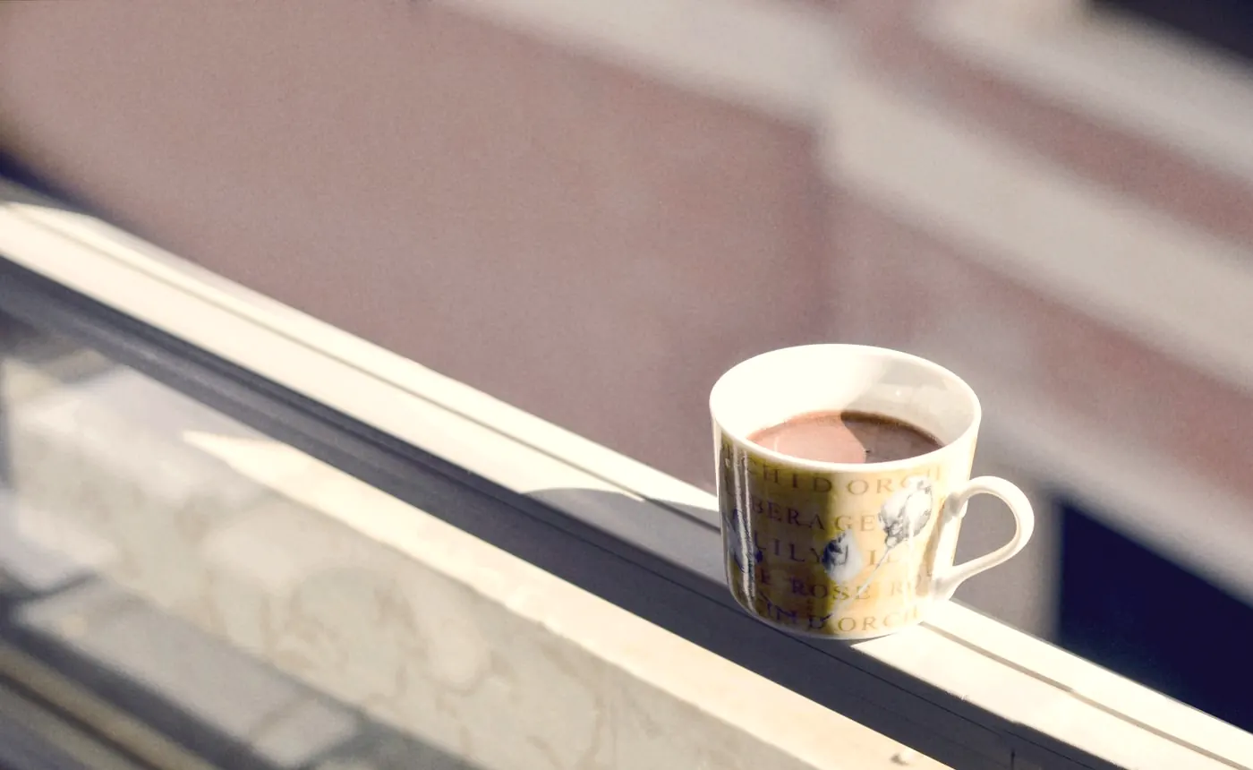 A cup of coffee on a balcony railing in warm morning light