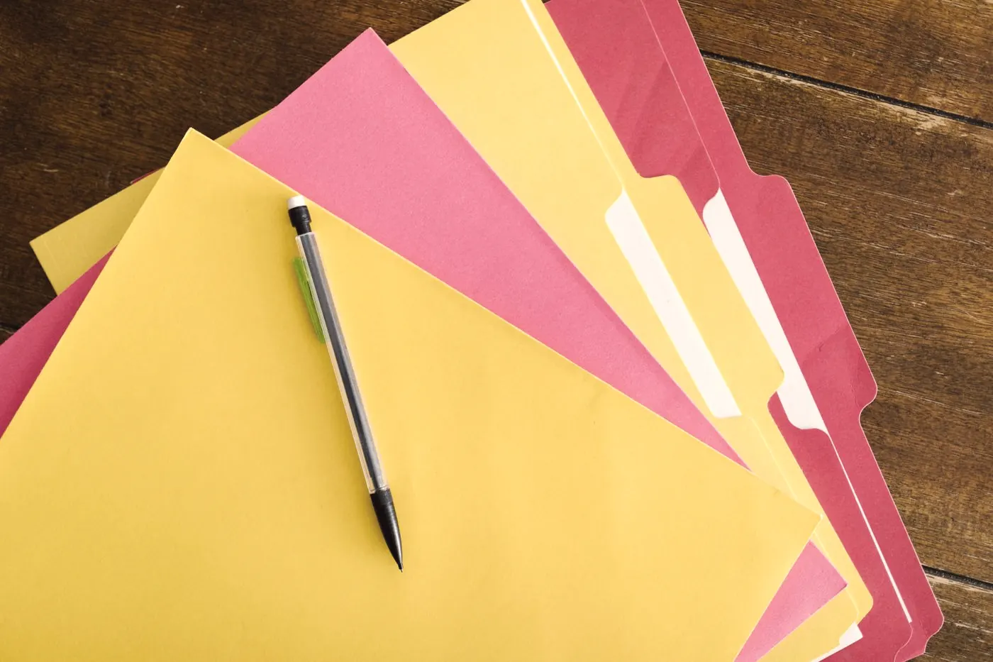 Colourful paper folders and a pen on a wooden table, sorting out who qualifies for cover