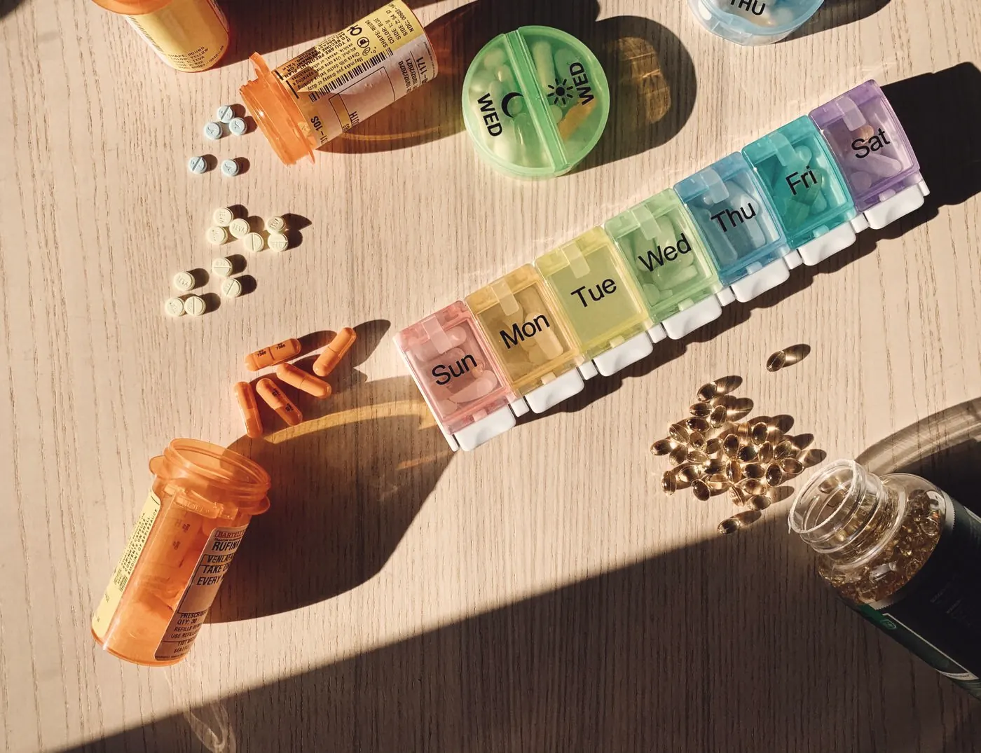 A colourful day-by-day pill organiser next to medicine bottles on a wooden table