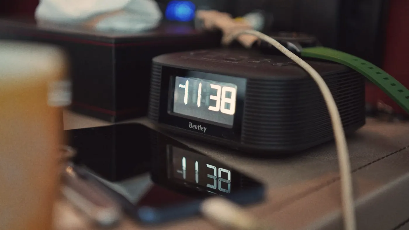 A digital bedside clock showing 11:38, reflected on a smartphone screen late at night