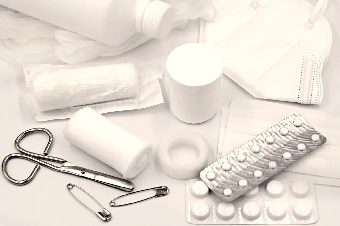 First aid supplies including bandage rolls, scissors and safety pins laid flat on a white surface