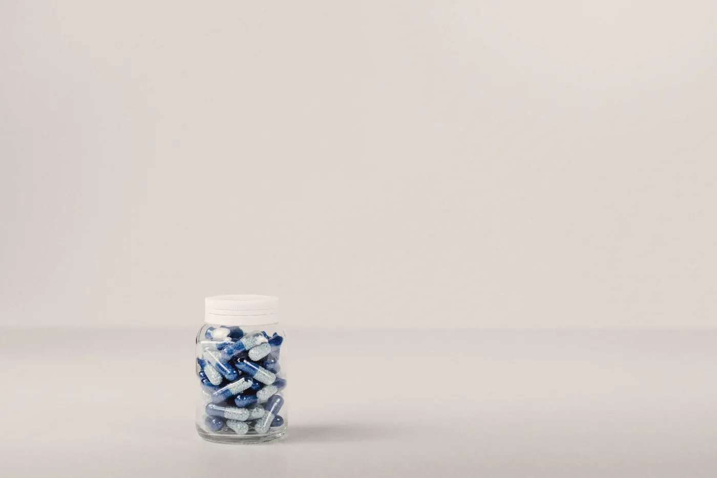 A small clear jar of tablets on a plain white surface