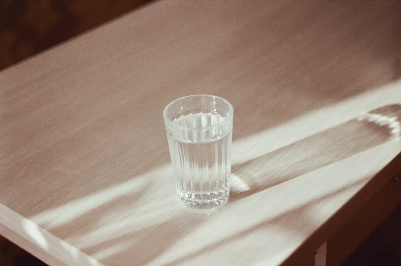 A glass of water on a sunlit wooden table, a reminder to keep drinking fluids on PEP