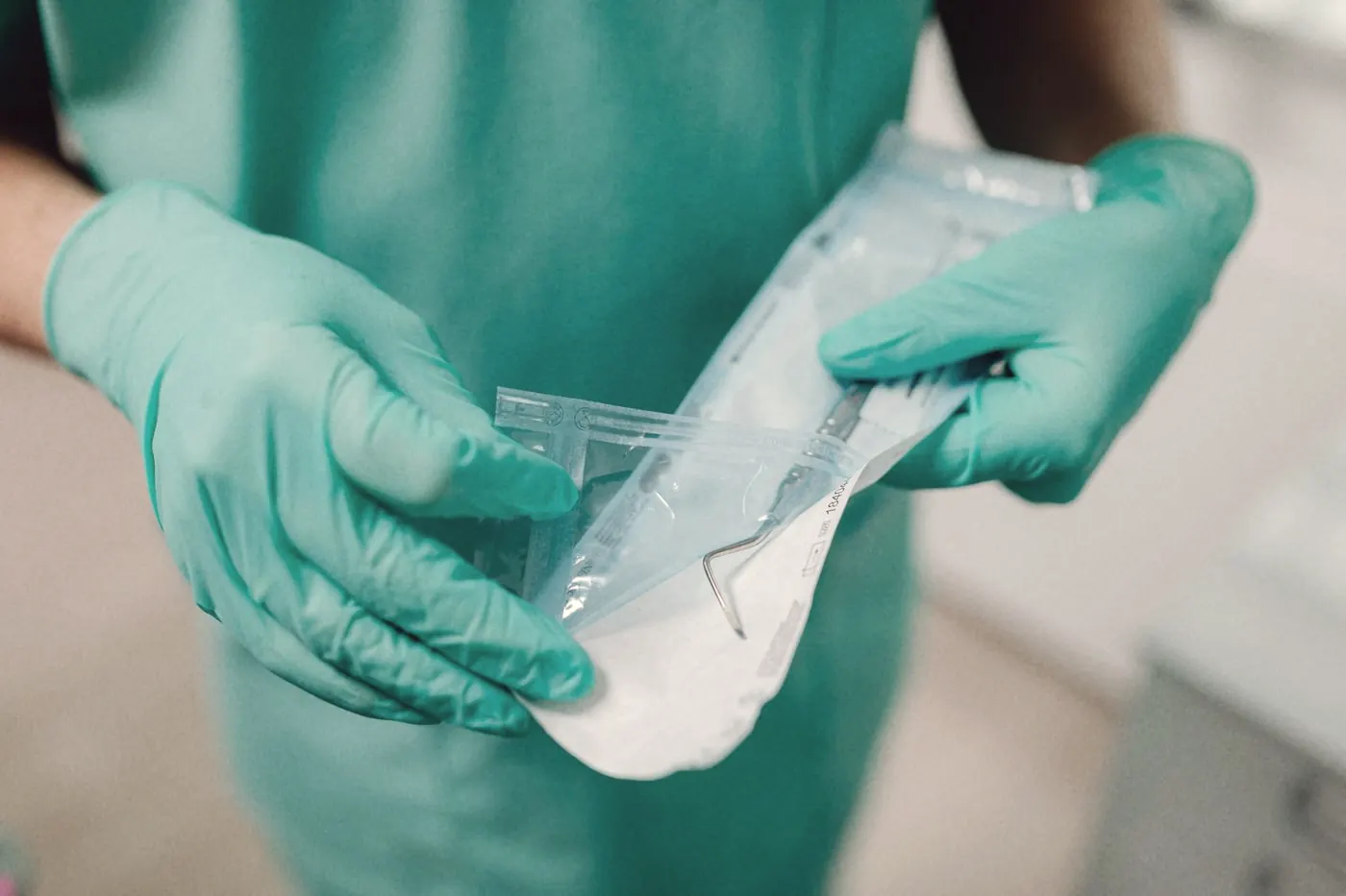 Gloved hands opening a sealed sterile instrument packet in a clinical room