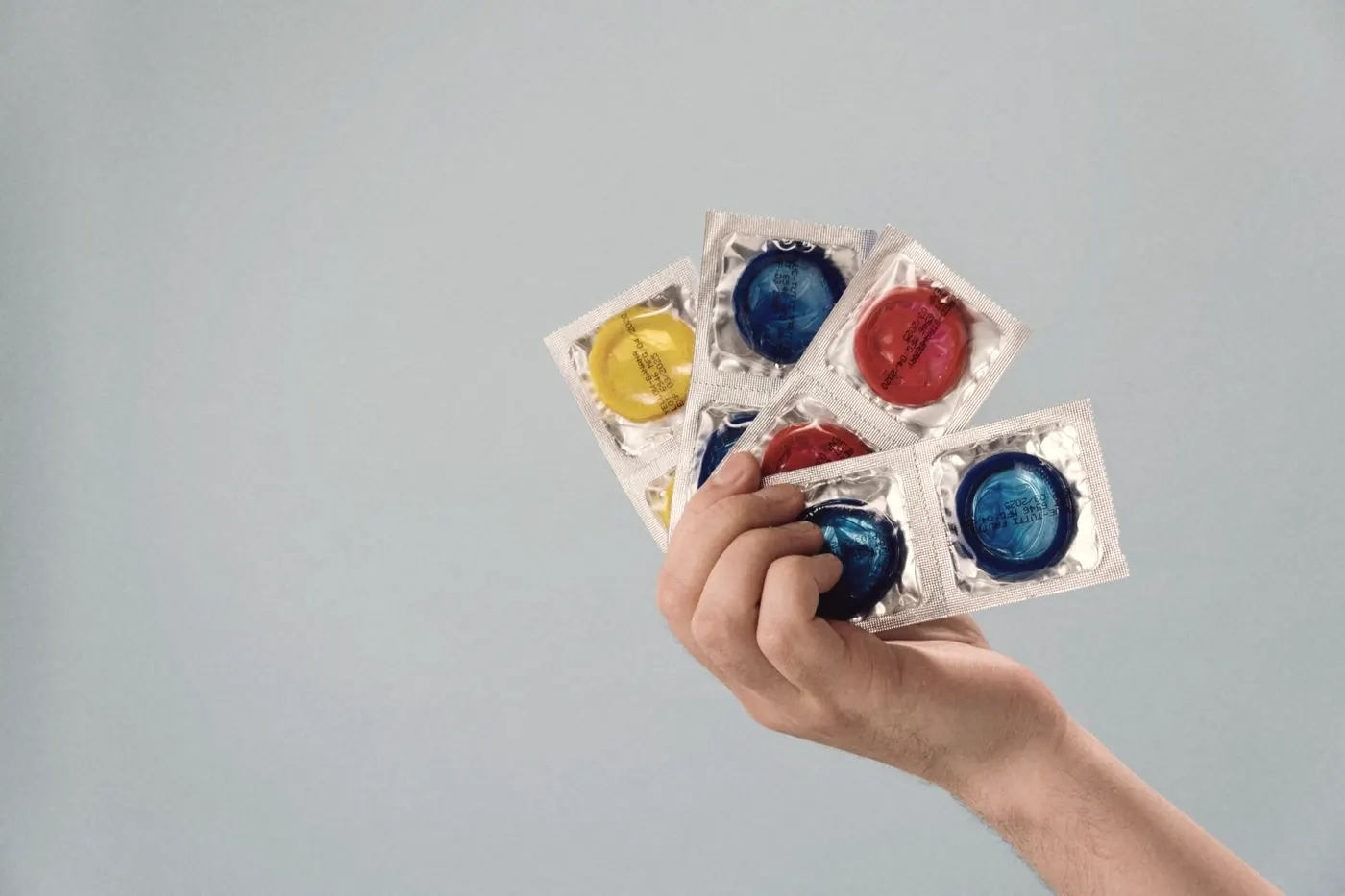 A hand holding colourful condom packets