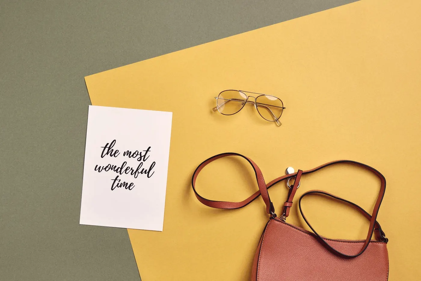 A small handbag and sunglasses laid out on a bright yellow and green background