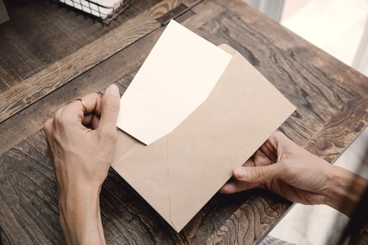 Hands taking a letter out of a brown envelope on a wooden desk, like a reply from an insurer