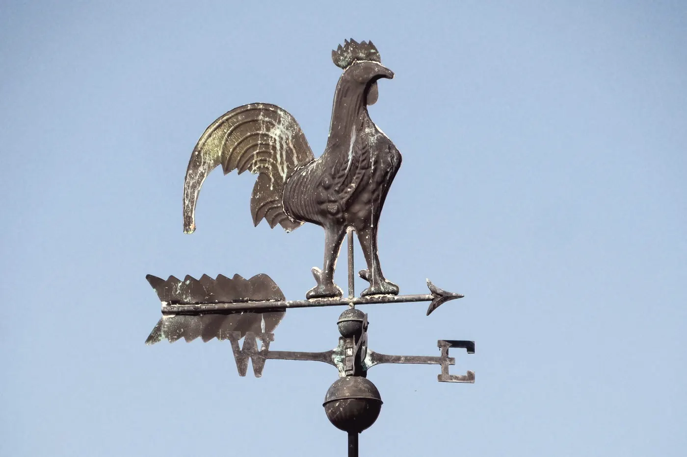 A bronze rooster weather vane against a pale blue sky, like a forecast that describes averages