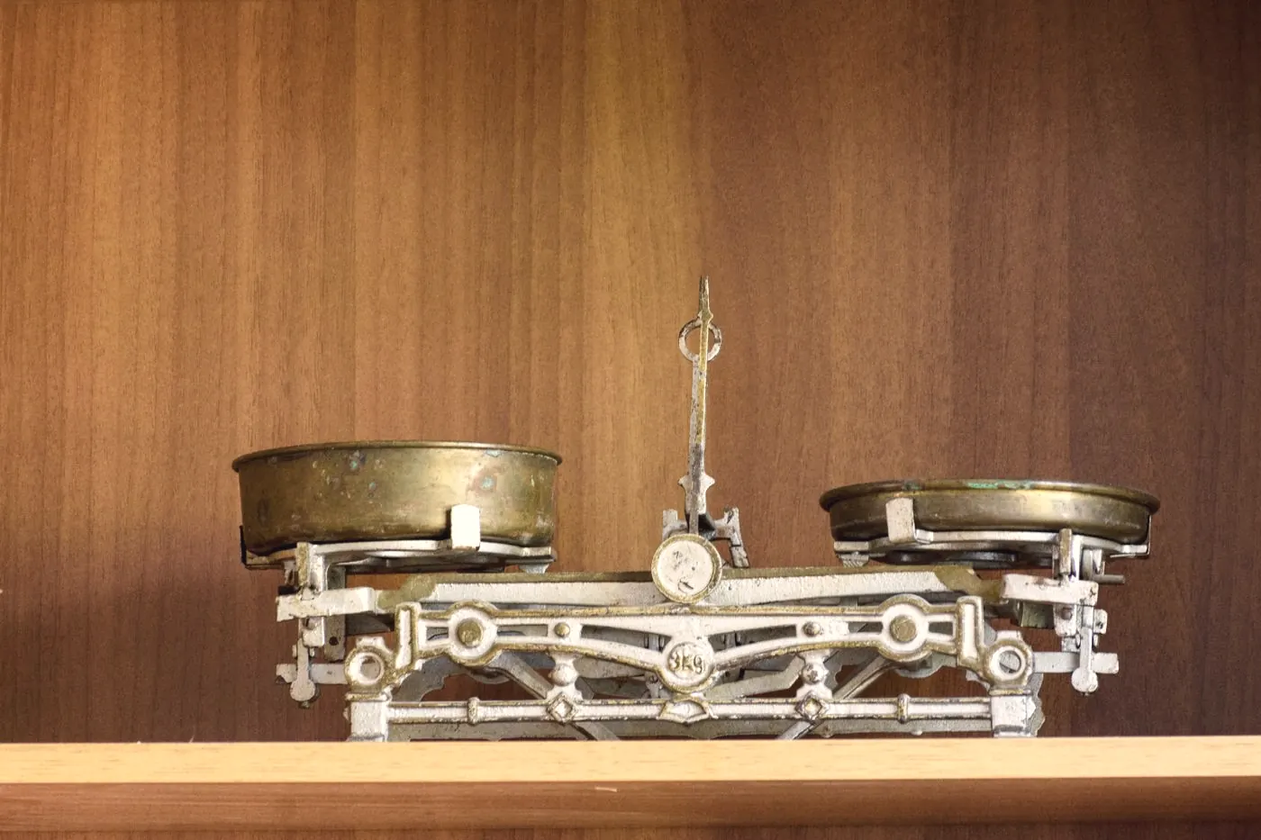A brass kitchen balance scale on a wooden shelf, weighing what raises or lowers the risk