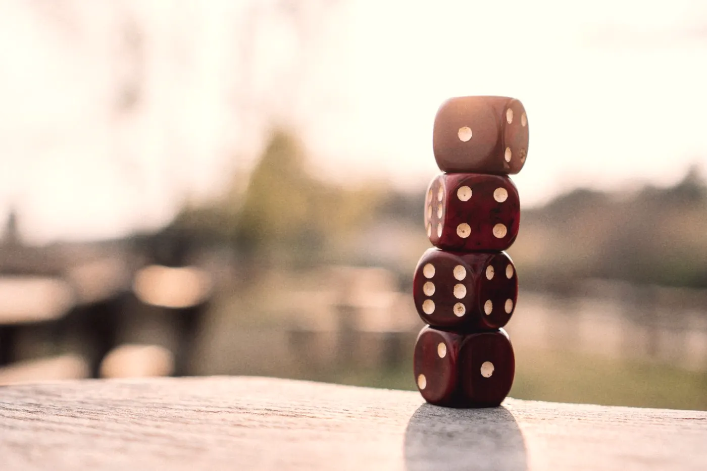 Four red dice stacked on a wooden table outdoors, a reminder that odds are not certainties
