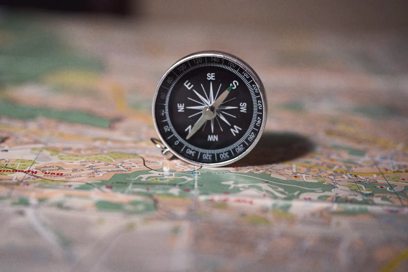 A black compass standing on a colourful map, reading direction rather than an exact route
