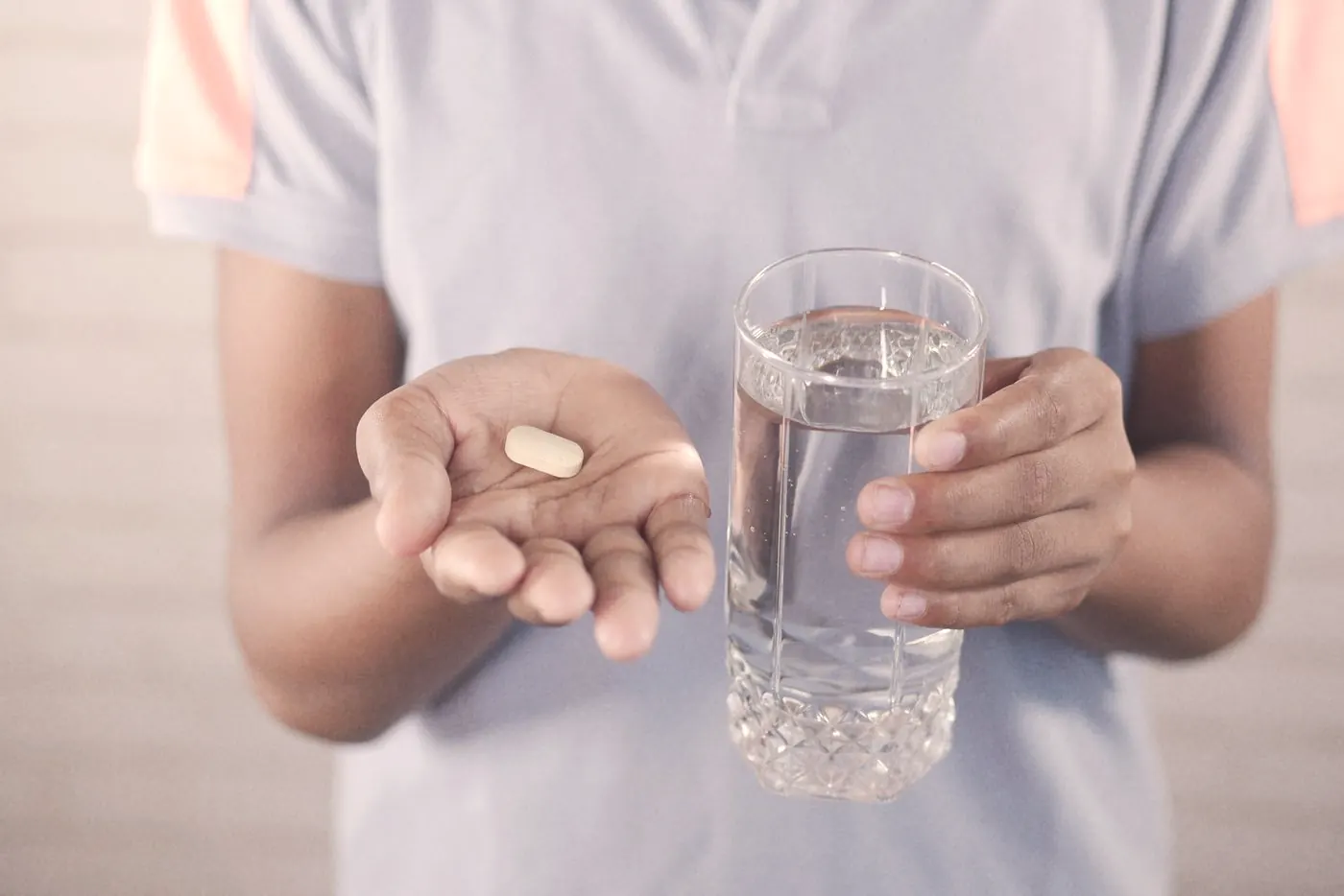 A person holding a single tablet and a glass of water, ready to take a late dose