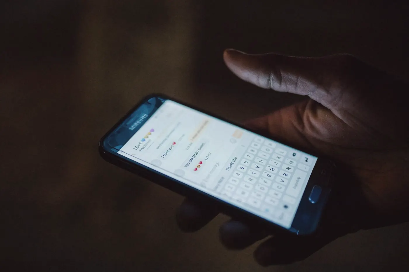 A hand holding a smartphone with a messaging app open in a dark room at night
