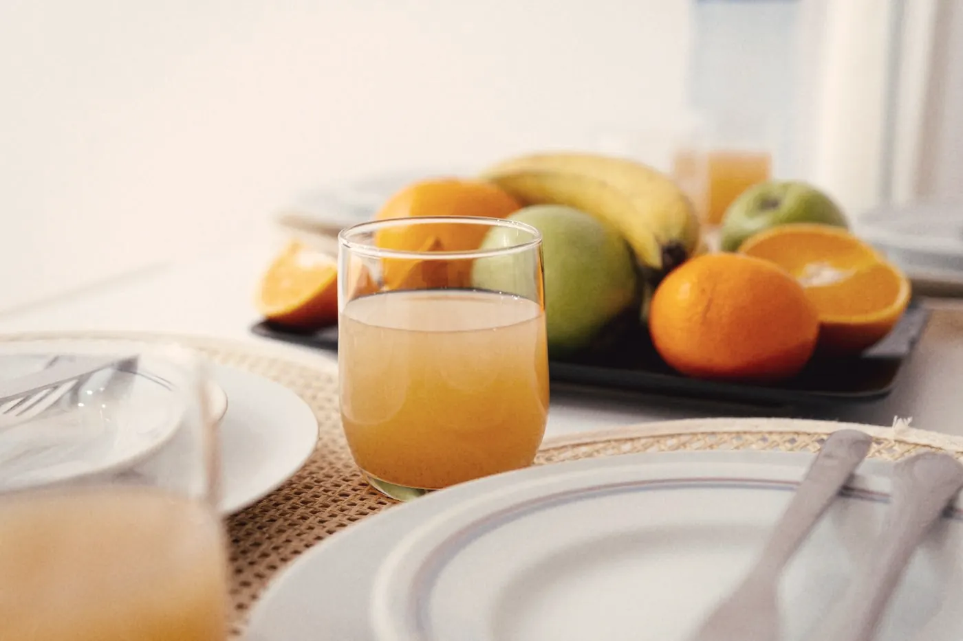 A bright breakfast table with orange juice and a bowl of fresh fruit