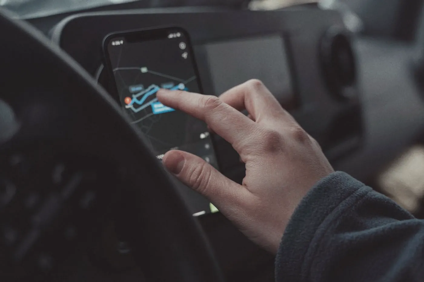 A hand using a map navigation app on a smartphone mounted inside a car