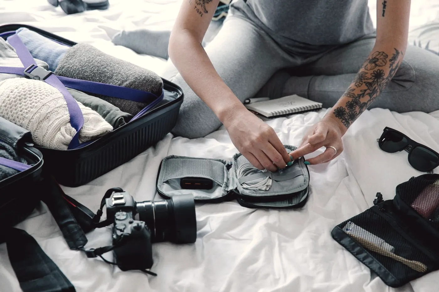 Hands packing a small travel pouch into an open suitcase alongside a camera