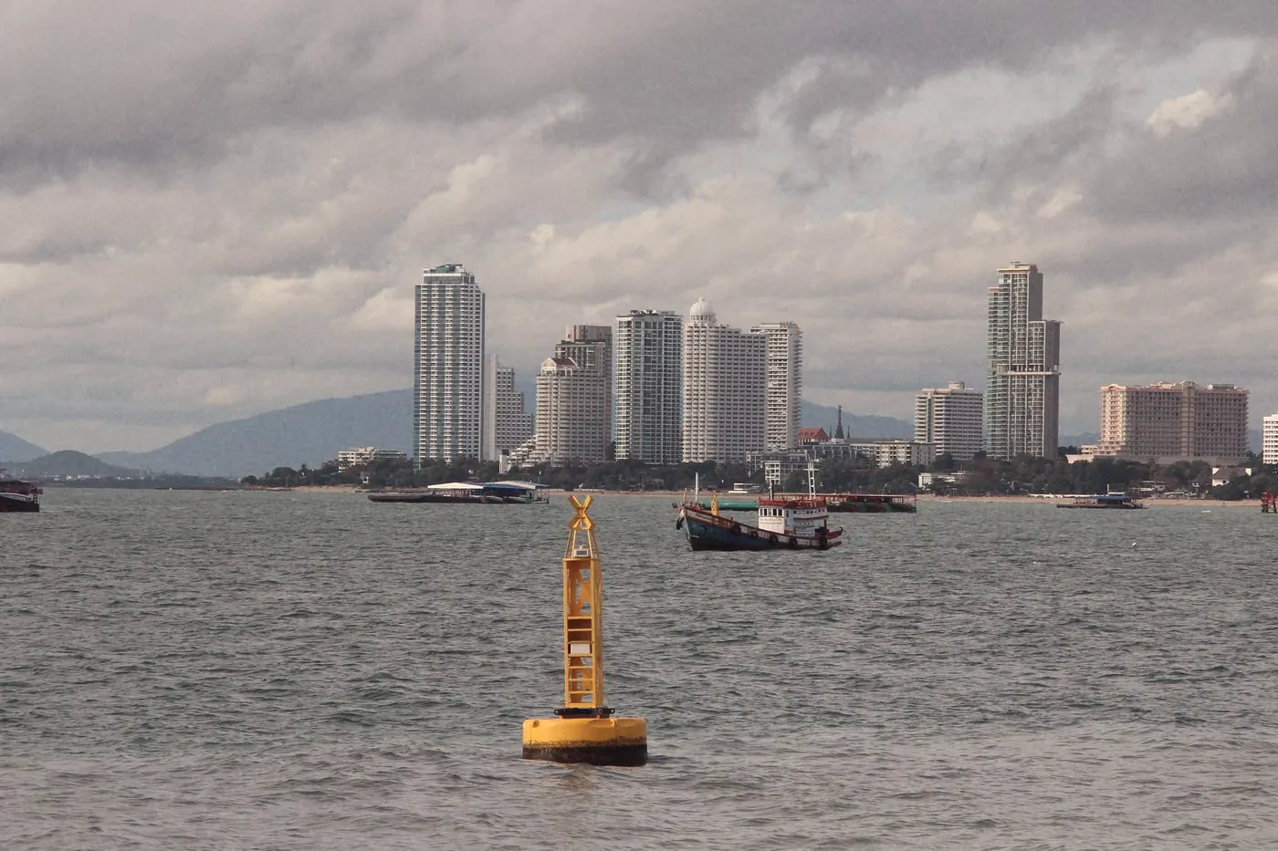 Pattaya skyline across the bay with small boats and a yellow buoy on a cloudy day