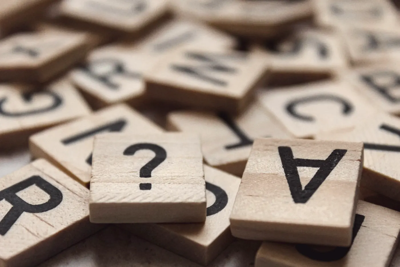 A wooden letter tile with a question mark among scattered letter tiles
