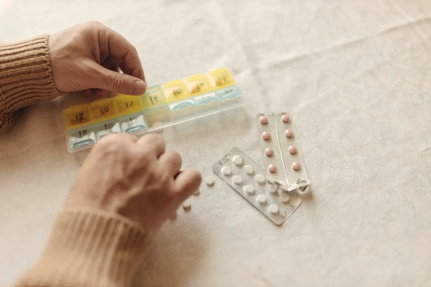 Hands filling a weekly pillbox to keep a daily PrEP routine