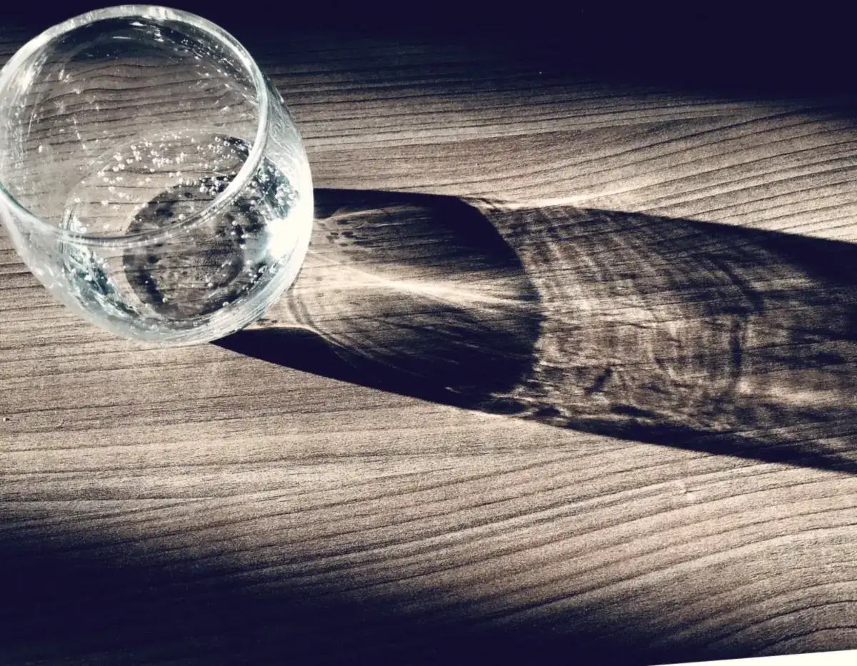 A glass of water casting a long shadow on a wooden table, a reminder to stay hydrated