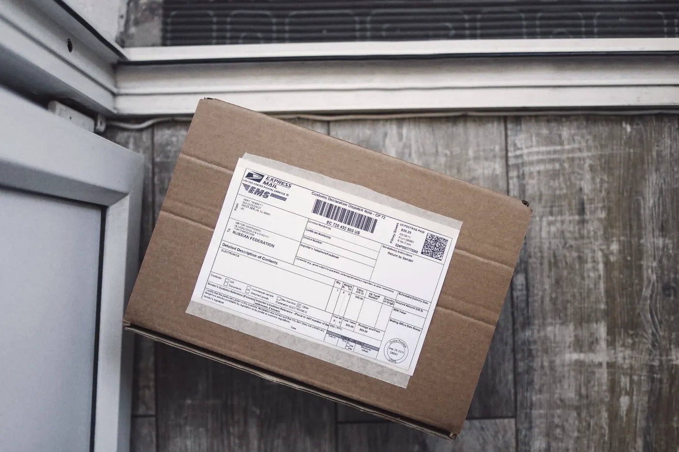 A cardboard parcel with a shipping label on the floor by a front door