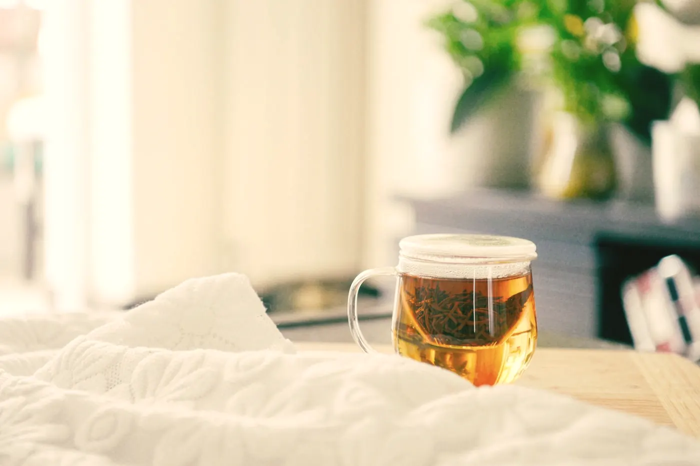 A glass mug of warm tea resting on a white blanket in a calm bedroom