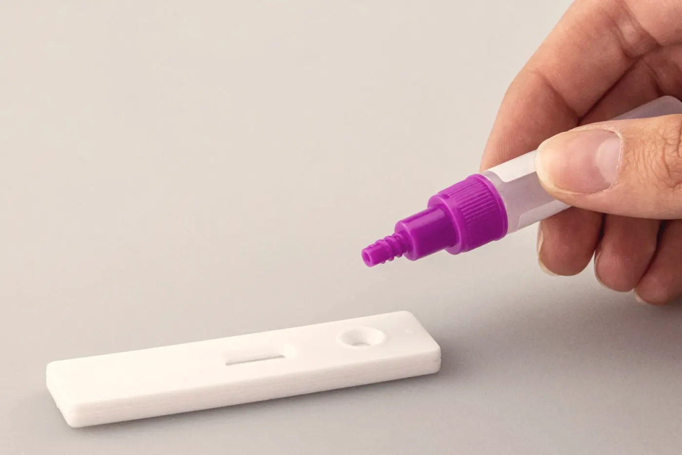 A hand adding buffer liquid from a dropper to a white rapid test cassette