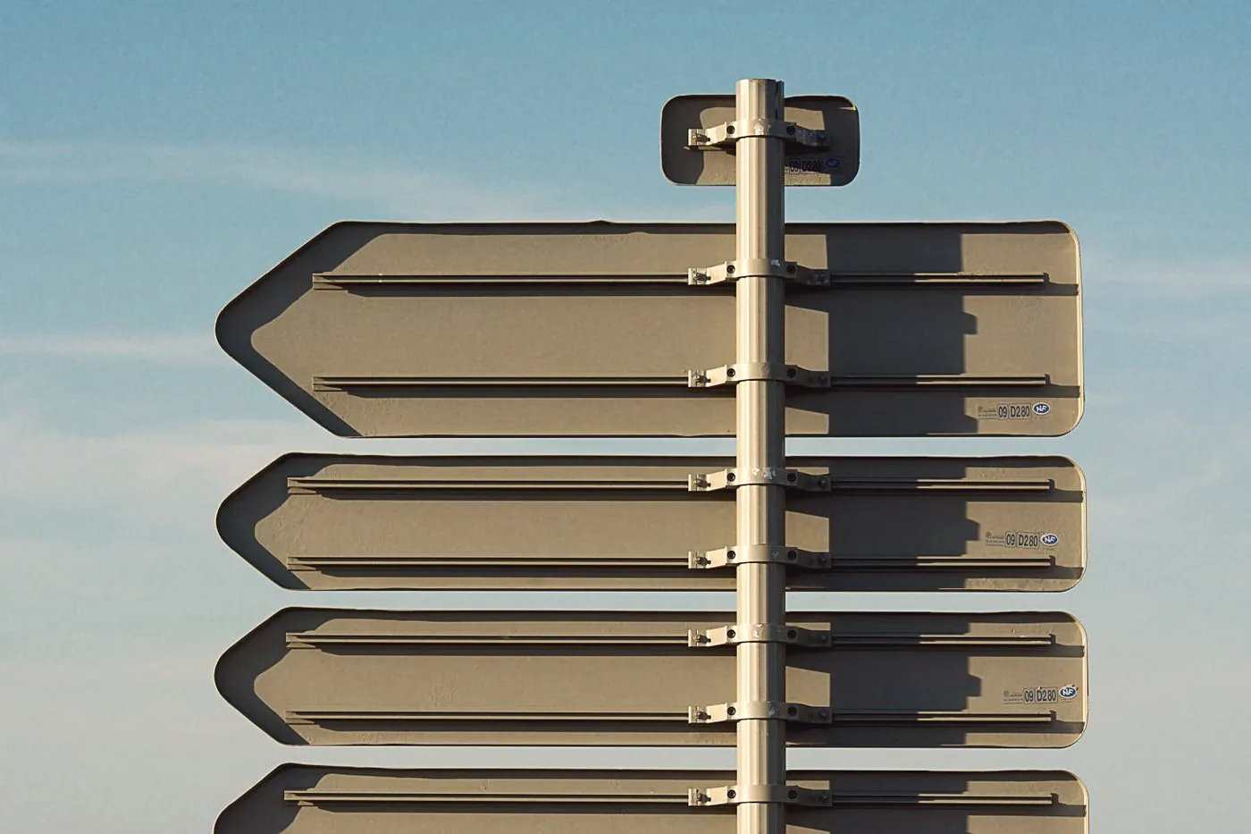 Several blank directional signposts pointing the same way under a blue sky