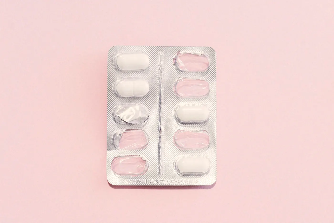 A single blister pack of white tablets on a soft pink background