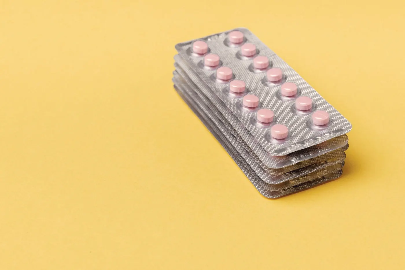 A stack of tablet blister packs on a yellow surface, like a 28-day course taken home