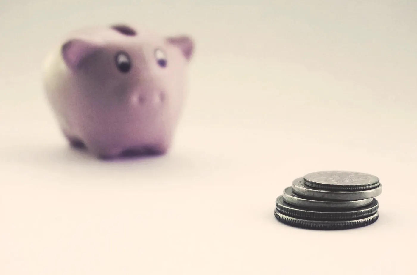 Stacked coins in front of a pink piggy bank, for budgeting the cost of STI tests