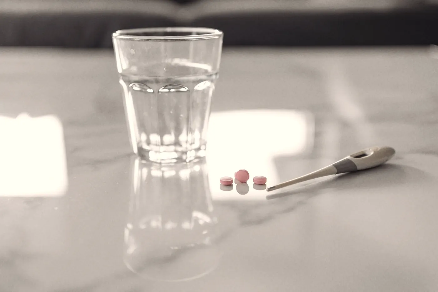 A digital thermometer, a glass of water and a few tablets on a marble table