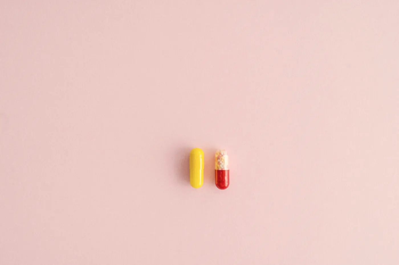 Two capsules, one yellow and one red, on a plain pink background