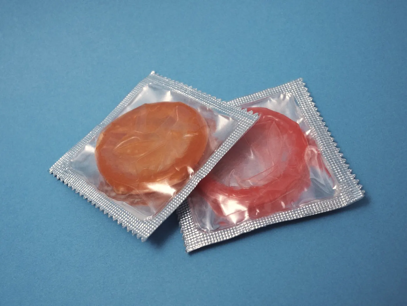 Two sealed condom packs on a plain blue background