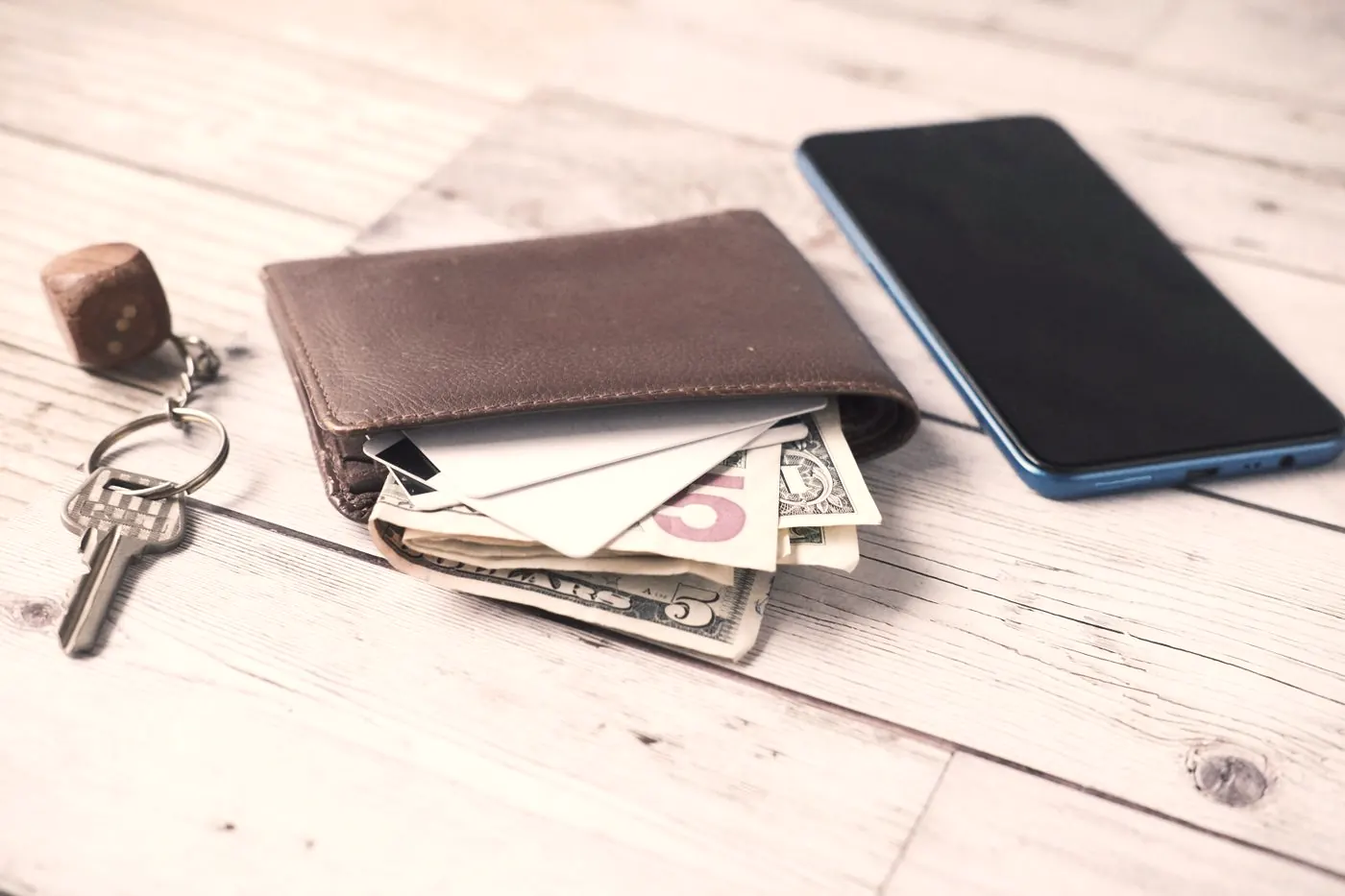 A wallet with cash, a smartphone and a set of keys laid out on a wooden table