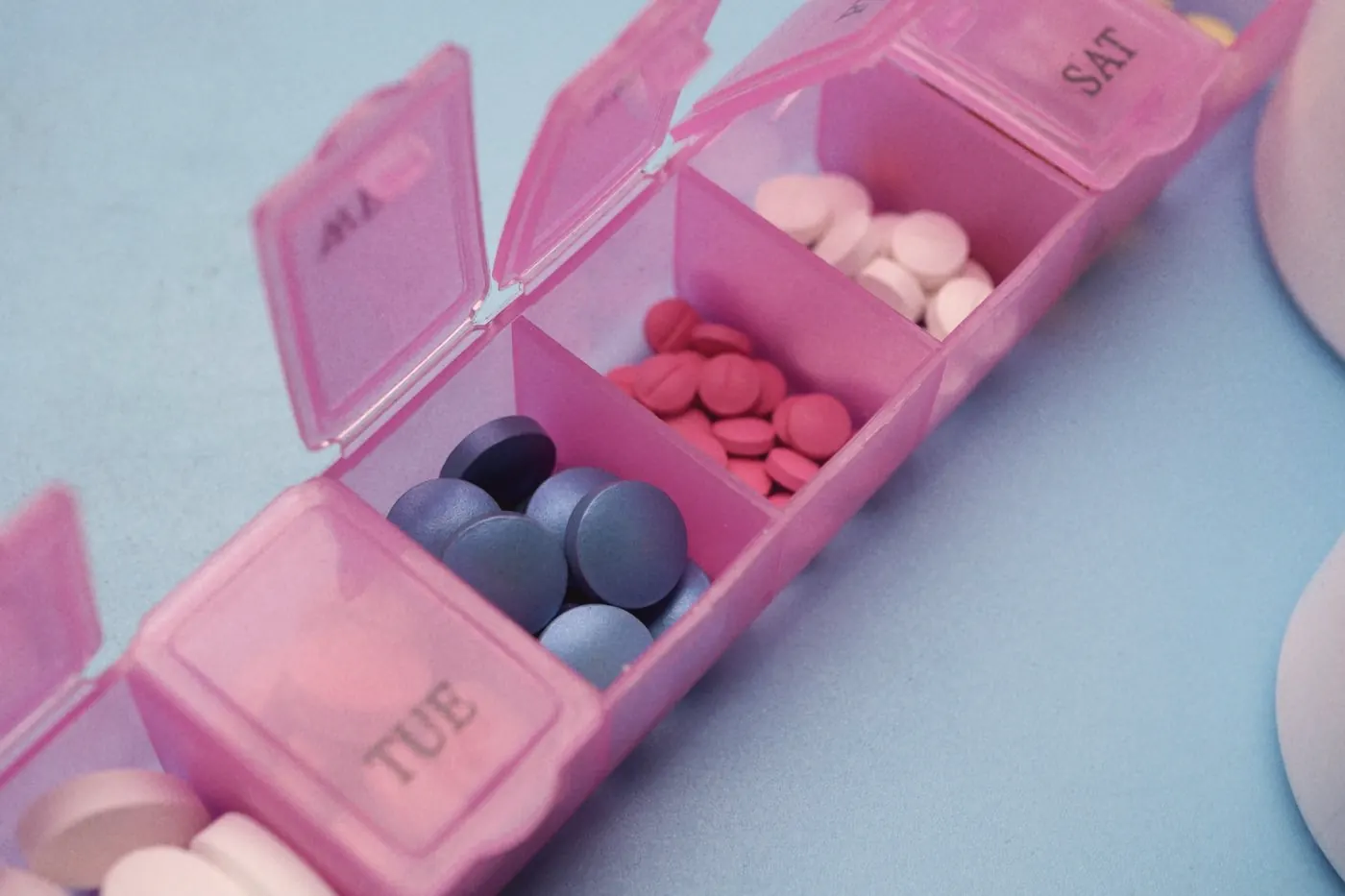 A pink weekly pill organiser with compartments of coloured tablets