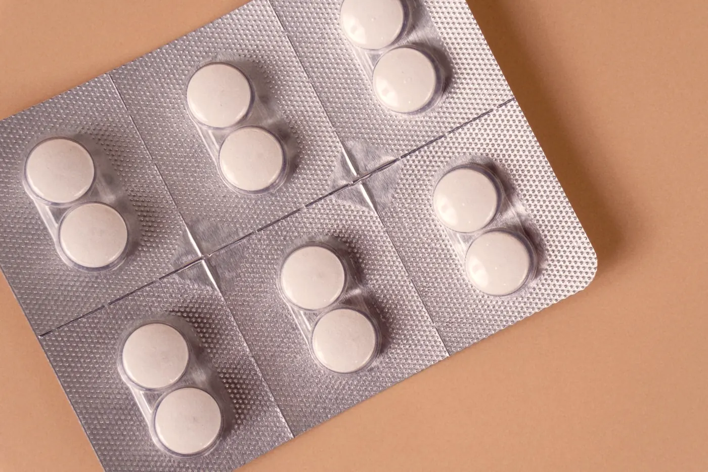 White tablets in a blister pack on a plain peach background