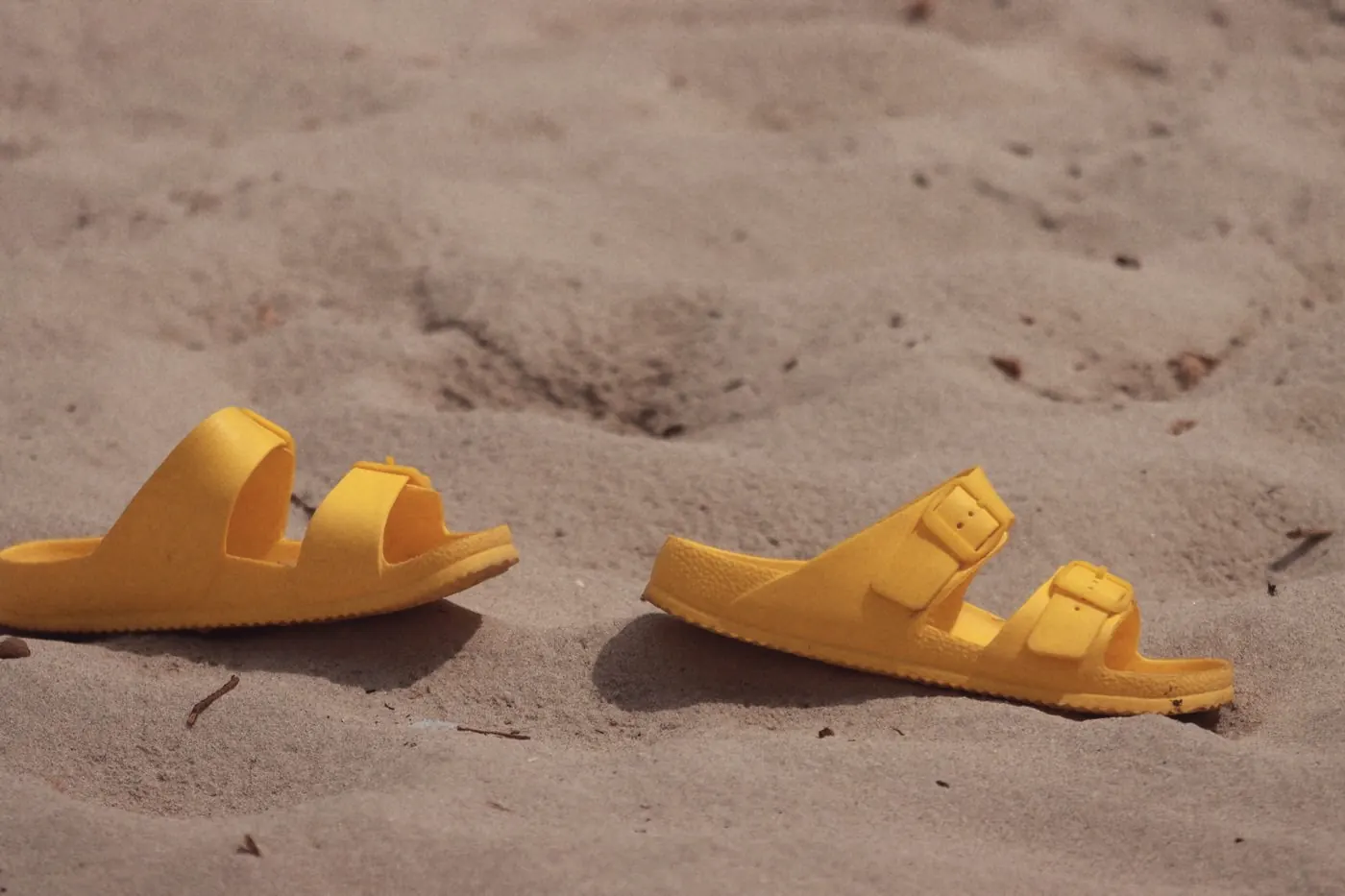 A pair of yellow sandals resting on soft sand on a sunny beach