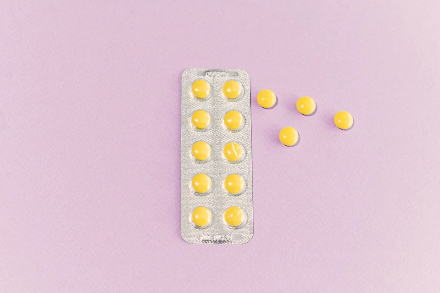 Yellow tablets in a blister pack with a few loose tablets on a purple surface